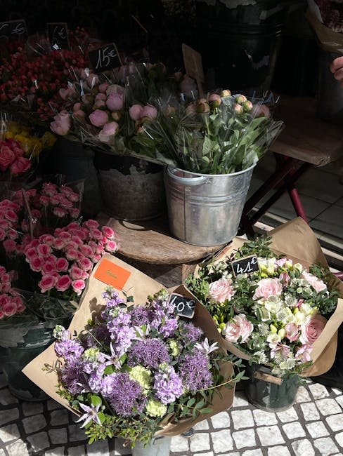 A display of fresh flower bouquets arranged for floral gifting at a flower shop, including a cluster of purple and lavender flowers with rounded blooms, a bouquet of pink and cream roses with lush gre